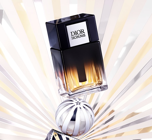 Dior Homme-Parfümflakon mit einem Farbverlauf von Schwarz zu Bernstein, positioniert über einer silbergestreiften Kugel und einer dekorativen Box. Der Hintergrund zeigt strahlende Sternstrahlen in Gold-, Silber- und Weißtönen.